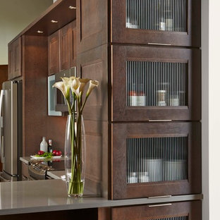 Mid-sized contemporary l-shaped separate kitchen in Orange County with brown cabinets, stainless steel appliances, solid surface benchtops, a peninsula and glass-front cabinets.