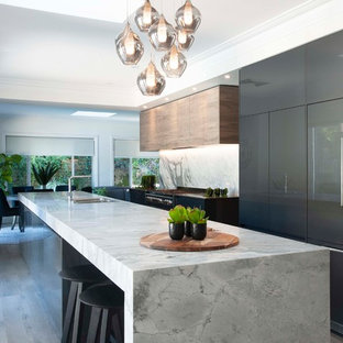 Design ideas for a large contemporary galley open plan kitchen in Sydney with a drop-in sink, marble benchtops, stone slab splashback, black appliances, with island, flat-panel cabinets, brown cabinets, grey splashback, medium hardwood floors, grey floor and grey benchtop.