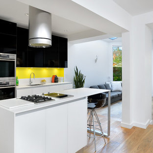 Ejemplo de cocina de galera, moderna, abierta, con fregadero bajoencimera, armarios con paneles lisos, puertas de armario negras, salpicadero amarillo, encimera de cuarcita, electrodomésticos de acero inoxidable, suelo de madera clara y una isla