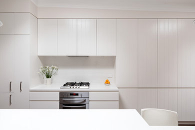 Foto på ett funkis vit kök, med en enkel diskho, bänkskiva i kvarts, vitt stänkskydd, rostfria vitvaror, mörkt trägolv, en köksö och brunt golv