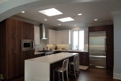 Mid-sized trendy l-shaped laminate floor eat-in kitchen photo in Other with flat-panel cabinets, medium tone wood cabinets, quartz countertops, an island, an undermount sink, white backsplash, stone slab backsplash and stainless steel appliances