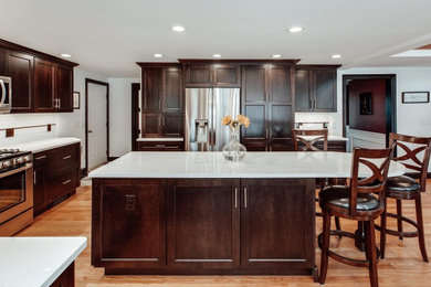 Kitchen - large transitional l-shaped light wood floor kitchen idea in Boston with an undermount sink, recessed-panel cabinets, dark wood cabinets, quartz countertops, white backsplash, subway tile backsplash, stainless steel appliances, an island and white countertops