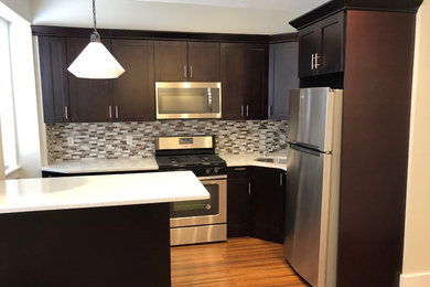 ニューヨークにある低価格の小さなコンテンポラリースタイルのおしゃれなキッチン (シングルシンク、シェーカースタイル扉のキャビネット、濃色木目調キャビネット、クオーツストーンカウンター、マルチカラーのキッチンパネル、モザイクタイルのキッチンパネル、シルバーの調理設備、淡色無垢フローリング、茶色い床、白いキッチンカウンター) の写真