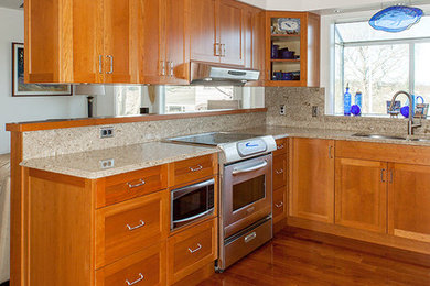 This is an example of a medium sized traditional u-shaped open plan kitchen in Vancouver with a submerged sink, shaker cabinets, medium wood cabinets, engineered stone countertops, beige splashback, stone slab splashback, stainless steel appliances, medium hardwood flooring, a breakfast bar and brown floors.