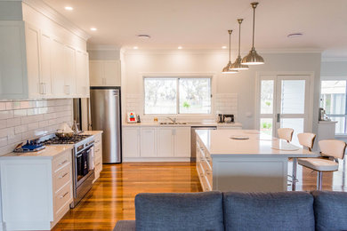 Example of a mid-sized transitional medium tone wood floor kitchen design in Other with a double-bowl sink, shaker cabinets, white cabinets, quartz countertops, white backsplash, ceramic backsplash, stainless steel appliances and an island
