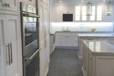 Example of a transitional l-shaped porcelain tile and gray floor kitchen design in Orange County with recessed-panel cabinets, white cabinets, granite countertops, stone slab backsplash, stainless steel appliances and two islands