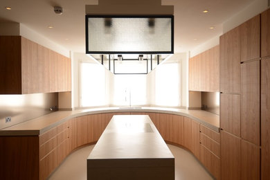 This is an example of a large contemporary u-shaped kitchen/diner in London with a built-in sink, flat-panel cabinets, light wood cabinets, concrete worktops, metallic splashback, concrete flooring and an island.