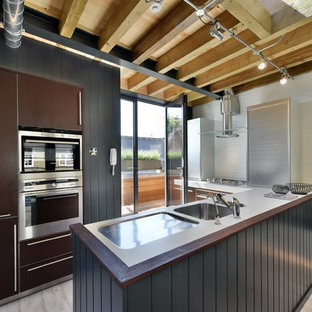 Photo of a medium sized contemporary kitchen in London with a submerged sink, flat-panel cabinets, brown cabinets, stainless steel appliances, a breakfast bar and white worktops.