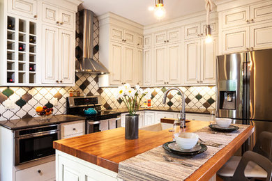 Example of a mid-sized transitional l-shaped medium tone wood floor and brown floor eat-in kitchen design in Denver with a farmhouse sink, raised-panel cabinets, multicolored backsplash, ceramic backsplash, stainless steel appliances, an island, white cabinets and solid surface countertops