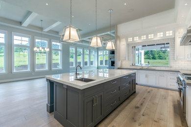 Example of a large trendy l-shaped medium tone wood floor and gray floor eat-in kitchen design in Portland with recessed-panel cabinets, white cabinets, marble countertops, white backsplash, stainless steel appliances, an island and white countertops