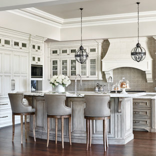 Modelo de cocina en L y bandeja, mediterránea, con armarios con rebordes decorativos, puertas de armario blancas, salpicadero verde, electrodomésticos con paneles, suelo de madera oscura, dos o más islas, suelo marrón y encimeras blancas