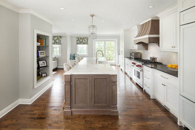 Example of a mid-sized transitional galley medium tone wood floor and brown floor open concept kitchen design in New York with a farmhouse sink, flat-panel cabinets, white cabinets, marble countertops, white backsplash, ceramic backsplash, stainless steel appliances, an island and white countertops
