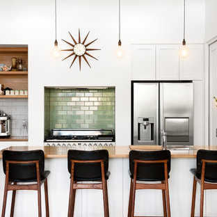 Photo of a contemporary galley kitchen in Adelaide with a drop-in sink, flat-panel cabinets, white cabinets, wood benchtops, green splashback, subway tile splashback, stainless steel appliances, a peninsula, beige floor and brown benchtop.