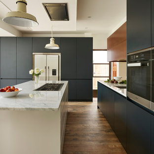 Inspiration for a large contemporary l-shaped eat-in kitchen in London with an integrated sink, blue cabinets, marble benchtops, metallic splashback, mirror splashback, light hardwood floors, with island, brown floor and white benchtop.