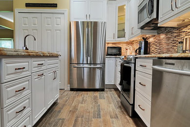Example of a transitional medium tone wood floor kitchen design in Miami with a farmhouse sink, raised-panel cabinets, white cabinets, granite countertops, ceramic backsplash, stainless steel appliances and an island