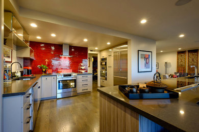 Mittelgroße Moderne Küche in L-Form mit Waschbecken, flächenbündigen Schrankfronten, Mineralwerkstoff-Arbeitsplatte, Küchenrückwand in Rot, Rückwand aus Glasfliesen, Küchengeräten aus Edelstahl, braunem Holzboden und Kücheninsel in Los Angeles