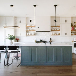 Transitional kitchen designs - Example of a transitional l-shaped dark wood floor and brown floor kitchen design in Denver with an undermount sink, shaker cabinets, white cabinets, white backsplash, an island and white countertops