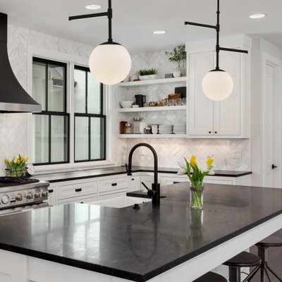 Example of a transitional l-shaped dark wood floor and brown floor kitchen design in Los Angeles with a farmhouse sink, shaker cabinets, white cabinets, white backsplash, stainless steel appliances, an island and black countertops