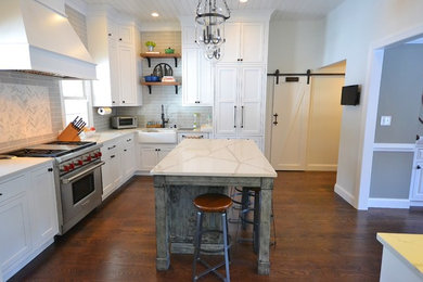 Huge transitional l-shaped dark wood floor and brown floor eat-in kitchen photo in Philadelphia with a farmhouse sink, recessed-panel cabinets, white cabinets, solid surface countertops, beige backsplash, subway tile backsplash, stainless steel appliances and an island