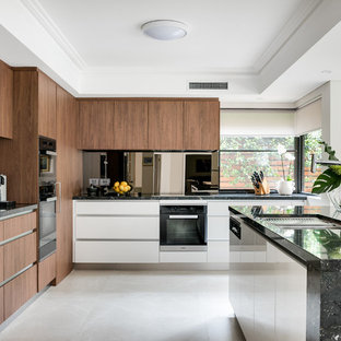 This is an example of a large contemporary l-shaped kitchen in Perth with an undermount sink, flat-panel cabinets, medium wood cabinets, black splashback, black appliances, with island, beige floor and black benchtop.