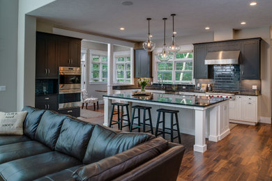 Large transitional single-wall medium tone wood floor open concept kitchen photo in Other with an undermount sink, shaker cabinets, gray cabinets, granite countertops, gray backsplash, ceramic backsplash, stainless steel appliances and an island