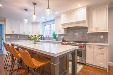 Eat-in kitchen - mid-sized transitional l-shaped medium tone wood floor and brown floor eat-in kitchen idea in New York with a farmhouse sink, beaded inset cabinets, white cabinets, solid surface countertops, gray backsplash, porcelain backsplash, stainless steel appliances, an island and white countertops