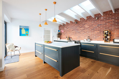 Photo of a large contemporary galley kitchen in Devon with an integrated sink, flat-panel cabinets, grey cabinets, red splashback, brick splashback, medium hardwood flooring, an island, beige floors and white worktops.