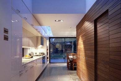 ロンドンにある中くらいなコンテンポラリースタイルのおしゃれなキッチン (フラットパネル扉のキャビネット、白いキャビネット、珪岩カウンター、白いキッチンパネル、ガラス板のキッチンパネル、シルバーの調理設備) の写真