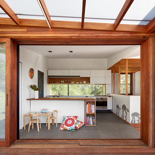 Design ideas for a midcentury kitchen in Wollongong with flat-panel cabinets, white cabinets, wood benchtops, window splashback, stainless steel appliances, concrete floors, a peninsula and grey floor.