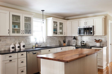 Example of a mid-sized transitional l-shaped light wood floor eat-in kitchen design in Other with an undermount sink, recessed-panel cabinets, beige cabinets, quartz countertops, multicolored backsplash, brick backsplash, stainless steel appliances, an island and black countertops