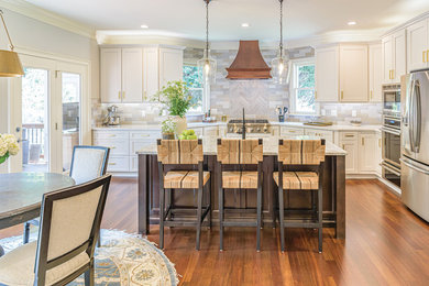 Example of a transitional l-shaped medium tone wood floor and brown floor kitchen design in Raleigh with shaker cabinets, white cabinets, gray backsplash, stainless steel appliances, an island and white countertops