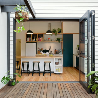 This is an example of a contemporary l-shaped kitchen in Melbourne with flat-panel cabinets, white cabinets, wood benchtops, white splashback, mosaic tile splashback, white appliances, medium hardwood floors, with island, brown floor and brown benchtop.
