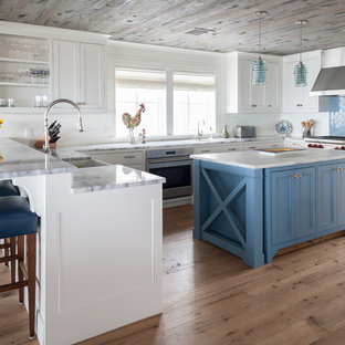 Inspiration for a coastal u-shaped medium tone wood floor and brown floor kitchen remodel in Bridgeport with a farmhouse sink, recessed-panel cabinets, white cabinets, blue backsplash, stainless steel appliances, an island and gray countertops