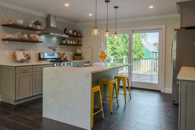 Example of a mid-sized trendy porcelain tile and brown floor kitchen design in New York with a farmhouse sink, beaded inset cabinets, gray cabinets, quartz countertops, gray backsplash, stone tile backsplash, stainless steel appliances and an island