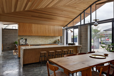メルボルンにあるミッドセンチュリースタイルのおしゃれなキッチン (フラットパネル扉のキャビネット、中間色木目調キャビネット、ベージュキッチンパネル、シルバーの調理設備、コンクリートの床) の写真