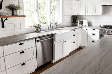 Eat-in kitchen - large cottage l-shaped medium tone wood floor and brown floor eat-in kitchen idea in Other with a farmhouse sink, shaker cabinets, white cabinets, marble countertops, white backsplash, stainless steel appliances, an island and gray countertops