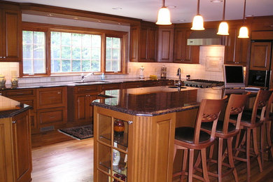 Inredning av ett stort kök, med luckor med upphöjd panel, skåp i mörkt trä, granitbänkskiva, beige stänkskydd, stänkskydd i porslinskakel, rostfria vitvaror, mellanmörkt trägolv och en köksö