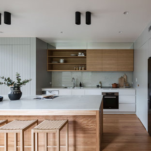 Photo of a large contemporary galley kitchen pantry in Sydney with an undermount sink, flat-panel cabinets, white cabinets, quartz benchtops, white splashback, engineered quartz splashback, black appliances, medium hardwood floors, with island and white benchtop.
