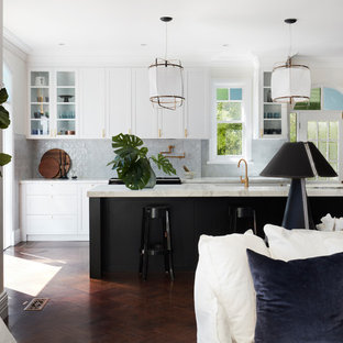 Photo of a transitional l-shaped open plan kitchen in Sydney with a farmhouse sink, shaker cabinets, black cabinets, grey splashback, black appliances, dark hardwood floors, with island and white benchtop.