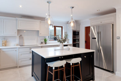 This is an example of a medium sized traditional l-shaped kitchen/diner in Kent with shaker cabinets, grey cabinets, quartz worktops, white splashback, stainless steel appliances, an island and white worktops.