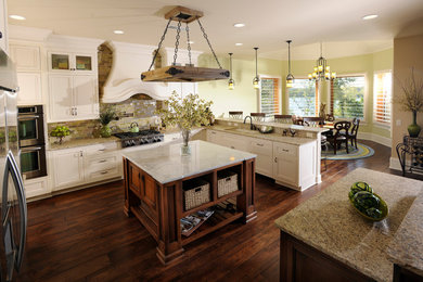 Inspiration for a mid-sized timeless u-shaped dark wood floor and brown floor enclosed kitchen remodel in Nashville with a double-bowl sink, shaker cabinets, white cabinets, granite countertops, multicolored backsplash, glass tile backsplash, stainless steel appliances and an island