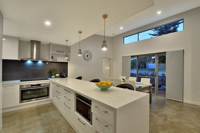 Exempel på ett litet modernt kök, med vita skåp, svart stänkskydd, betonggolv, grått golv, släta luckor, granitbänkskiva, stänkskydd i keramik, rostfria vitvaror och en halv köksö
