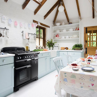 Design ideas for a country l-shaped eat-in kitchen in Melbourne with a farmhouse sink, shaker cabinets, blue cabinets, white splashback, black appliances, painted wood floors, no island, white floor and white benchtop.