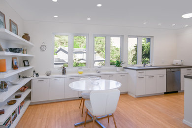 Example of a mid-sized trendy single-wall eat-in kitchen design in San Francisco with flat-panel cabinets, white cabinets, a peninsula, gray countertops and stainless steel appliances