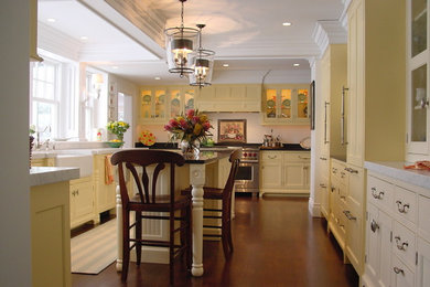 Enclosed kitchen - large traditional u-shaped dark wood floor enclosed kitchen idea in Portland Maine with a farmhouse sink, beaded inset cabinets, yellow cabinets, marble countertops, white backsplash, stone slab backsplash, paneled appliances and an island