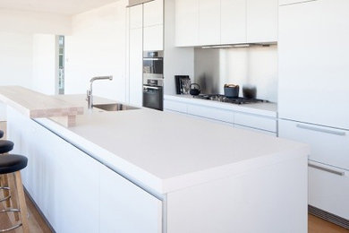 Inspiration for a modern medium tone wood floor kitchen remodel in Vancouver with an integrated sink, flat-panel cabinets, white cabinets, stainless steel appliances and an island