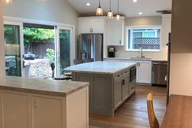 Inspiration for a large transitional medium tone wood floor and brown floor kitchen remodel in San Francisco with an undermount sink, shaker cabinets, white cabinets, quartzite countertops, beige backsplash, ceramic backsplash, stainless steel appliances, an island and white countertops