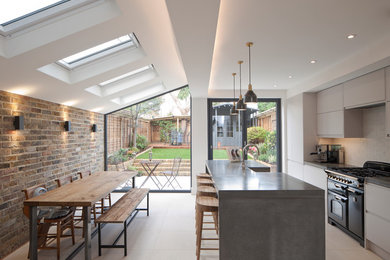 This is an example of a medium sized contemporary single-wall kitchen/diner in London with flat-panel cabinets, grey cabinets, concrete worktops, white splashback, brick splashback, black appliances, an island and white floors.