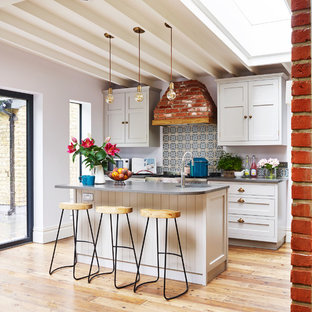 Idee per una cucina parallela design con lavello sottopiano, ante in stile shaker, ante bianche, paraspruzzi multicolore, elettrodomestici in acciaio inossidabile, pavimento in legno massello medio, isola e pavimento marrone