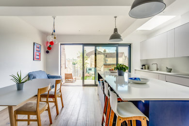 Inspiration for a large contemporary single-wall open plan kitchen in Other with an integrated sink, flat-panel cabinets, white cabinets, composite countertops, white splashback, engineered quartz splashback, stainless steel appliances, light hardwood flooring, an island, beige floors and white worktops.